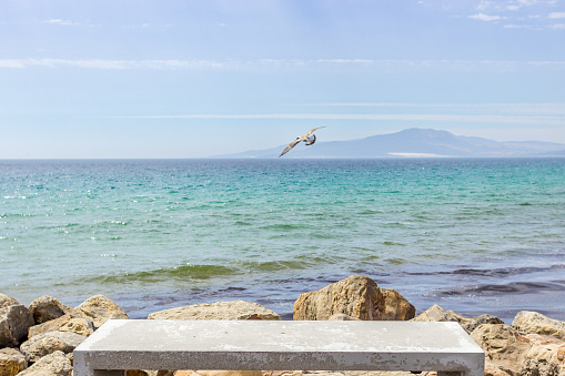 Stone bench on the seashore. Ocean view. Island on the horizon. Euro-trip. Strait of Gibraltar. Mediterranean Sea. A place for reflection. Empty bench. Holidays on the sunny coast.