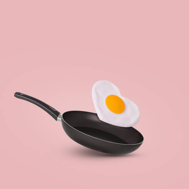 istock Creative idea with a frying pan and a flying fried egg in heart shape on a bright pink background. 1366851875
