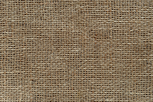 Burlap fabric texture macro. Background of coarsely woven sackcloth from jute, hemp or flax. Design element for rustic country style. Brown tan Ñanvas cloth as craft material. Top view.