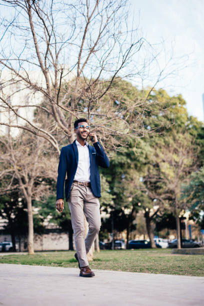 istock Wide shot smiling black man entrepreneur walking through a park while using his phone doing business 1366857161