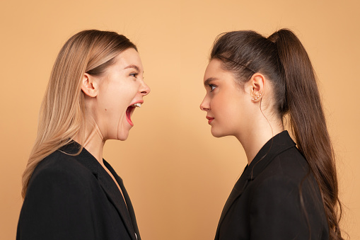 Boss yelling at employee. Colleague screaming on worker. Bulling on work. One woman shouting another woman facing each other face to face standing isolated color background. Side view