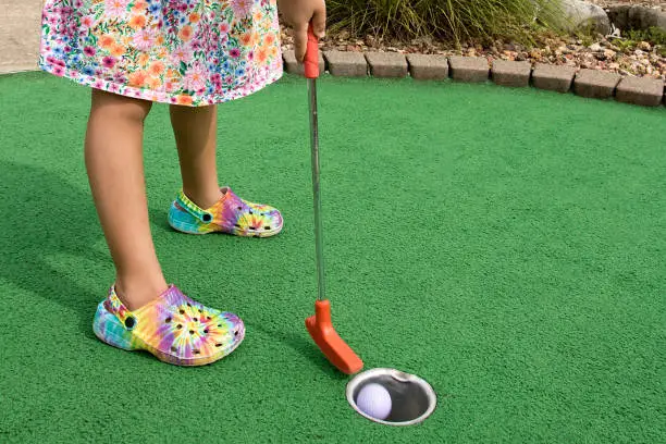 Gradeschooler wearing flowered dress putting on Miniature Golf course in summer.