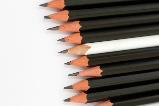 White pencil in a group of black pencils White pencil in a group of black pencils aligned, characterizing difference and diversity diversidade stock pictures, royalty-free photos & images