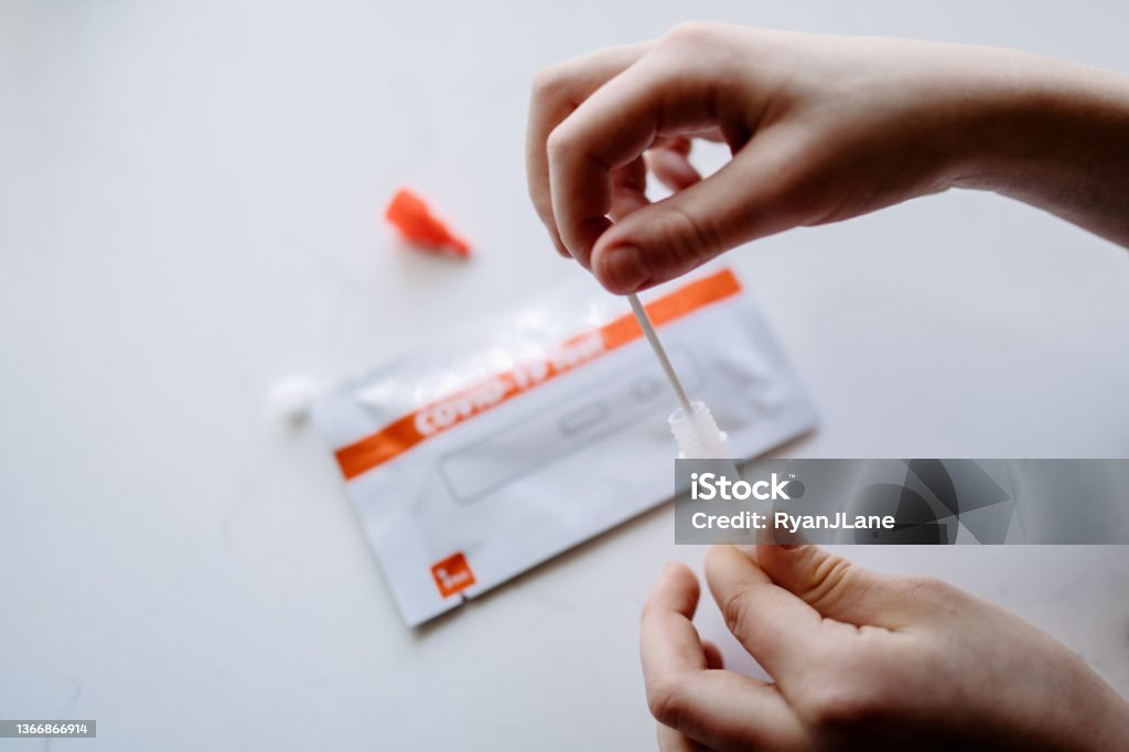 Person Using Home COVID Test Kit A persons hands taking a COVID-19 / Coronavirus home testing kit, meant to speed up results and prevent exposure and spread among infected individuals. Testing Kit Stock Photo