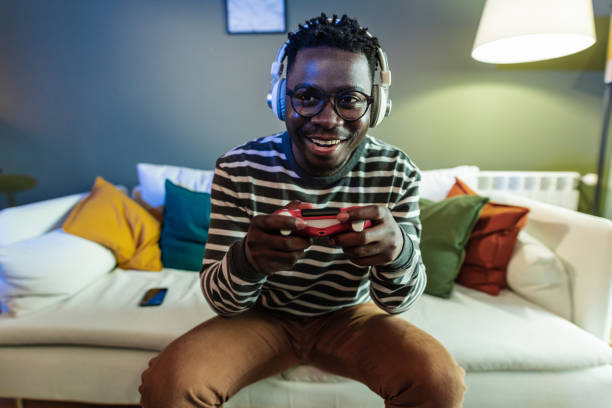 Young man playing video games at home A young African-American man is at home on the couch, he is having fun playing video games gamer stock pictures, royalty-free photos & images