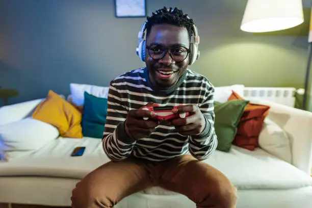 A young African-American man is at home on the couch, he is having fun playing video games