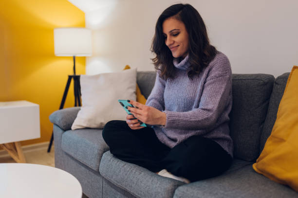 istock Hispanic woman using smartphone while sitting on the couch at home 1366871471