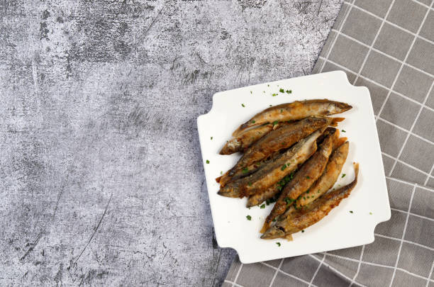 istock Pan fried capelin or smelt fish on a white square  plate on a dark background. Top view, flat lay 1366887341