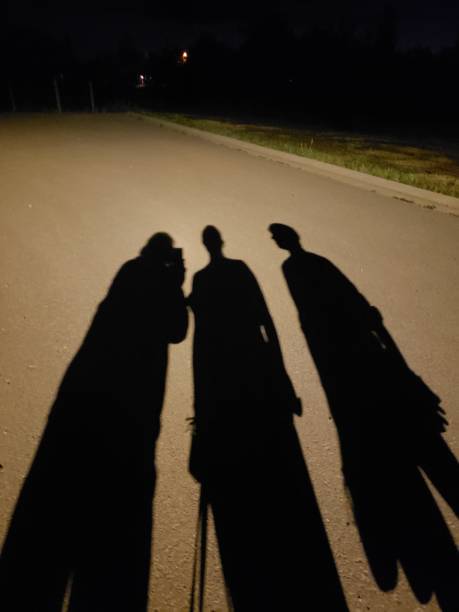 Shadows of three people on an asphalt road at night.