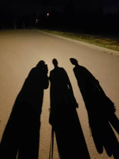 Photo of Shadows of three people on an asphalt road at night