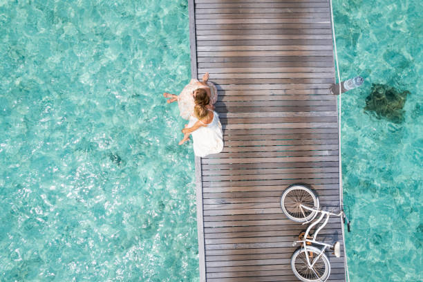 Two friends sitting side by side on jetty Two friends sitting side by side on jetty with bicycle jetty aerial stock pictures, royalty-free photos & images