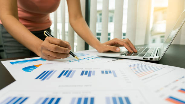 istock Businessman holding a profitability statistics analysis pen from a graph document in hand with a calculator and laptop on the table to plan profit growth from the past year. 1366894177