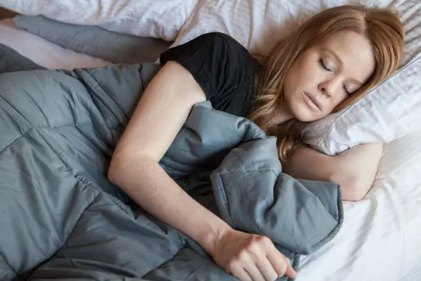 Photo of Young redhead woman using soft weighted blanket in her modern apartment