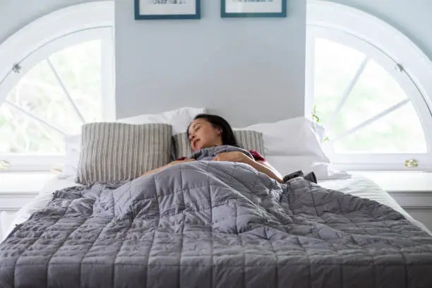 Photo of Woman sleeps under weighted blanket in bright bedroom