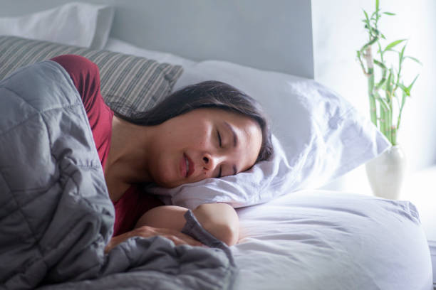 Woman sleeps under weighted blanket in bright bedroom stock photo