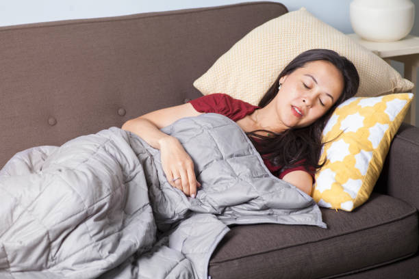 Woman sleeps and takes a nap on a couch with a gray weighted blanket stock photo