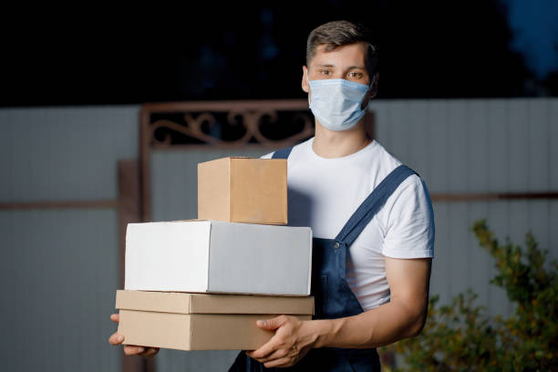 istock Courier man in uniform and mask holds a stack of boxes in his hands. Courier delivery service with parcels in hand in the open air 1366904361