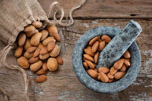 Photo of Many almonds in the stone mortar and sack bag.