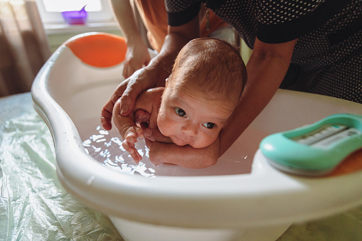 Mother and grandmother bathing newborn baby in a baby bath. Baby hygiene and care