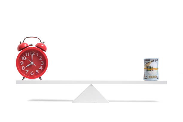 istock Red alarm clock and roll hundred dollar bills are balanced scale white background. 1366915789