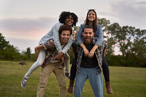 Three-quarter length front view of Black, African-American, and Hispanic men and women in casual clothing standing together in open field and smiling at camera.