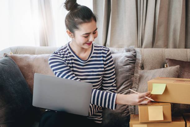 istock Online merchandising business idea, a beautiful girl is writing a notebook and using a computer to check the order to deliver parcels to customers according to orders received from customers. 1366916779