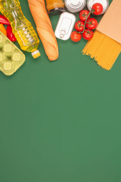 istock Vertical image with groceries, food donations on green background with copy space - pasta, vegatables, canned food, baguette, cooking oil, tomatoes. Food bank, food delivery concept 1366917749