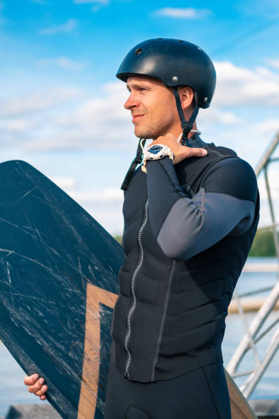 istock Focused wakeboarder in full gear standing on pier with board, intently looking away 1366917802