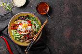 Traditional Korean dish Bibimbap. Bowl with rice, shiitake mushrooms, chicken, cucumber and microgreens and Korean bibimbap sauce top view. Dark background, copy space for text