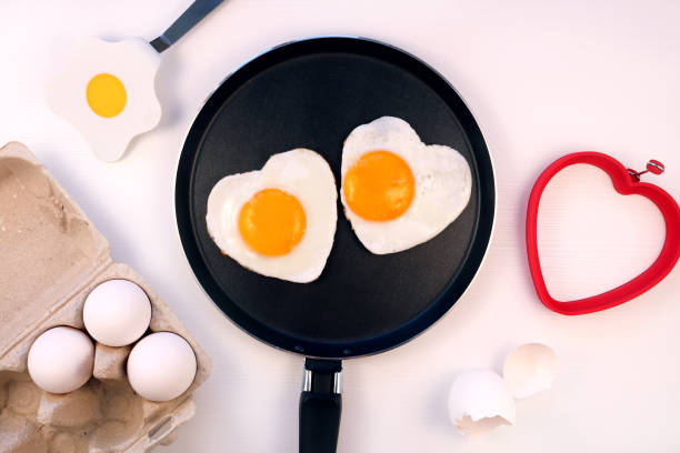 istock Heart shaped fried eggs on a pan, white background, top view. Valentines day breakfast idea. 1366919219