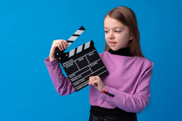 istock Smiling girl holding clapper board against blue background 1366922408