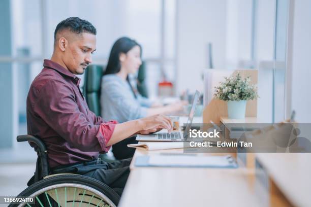 Asian Indian White Collar Male Worker In Wheelchair Concentrating Working In Office Beside His Colleague Stock Photo - Download Image Now