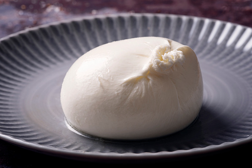 Close-up view of a ball of burrata cheese. Burrata cheese is recognisable  by its loose texture: small, soft cheese curds and cream packed inside an outer shell similar to mozzarella. Colour, horizontal format with some copy space.