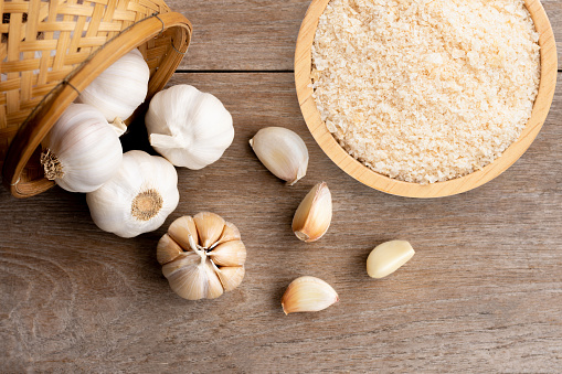 Garlic powder in wooden bowl and bulb of garlic isolated on wooden table background. Top view. Flat lay.