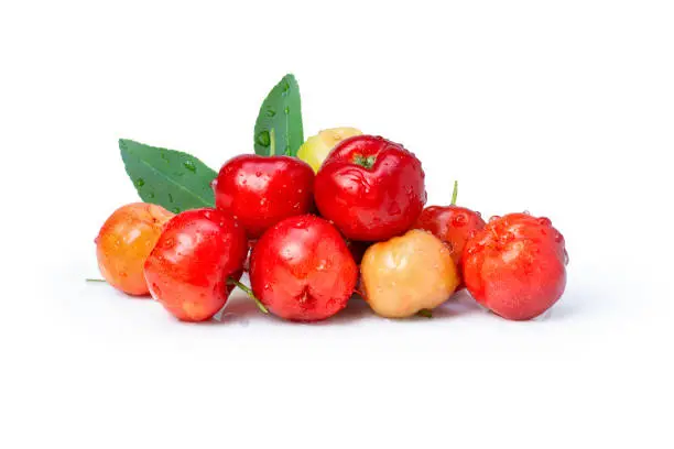 Pile of fresh red acerola cherry fruit ( Malpighia Glabra ) with green leaves isolated on white background