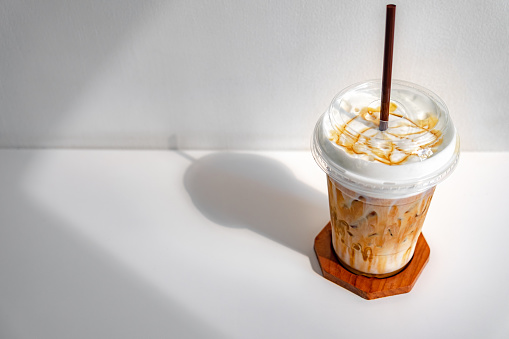 Iced caramel macchiato coffee in plastic cup on a wooden table at the cafe. Cold espresso in the coffee shop with copy space. Beverage glass frozen in the restaurant. Food interior decoration vintage.