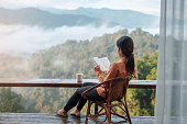 istock young woman reading book near window and looking mountain view at countryside homestay in the morning sunrise. SoloTravel, journey, trip and relaxing concept 1366932733