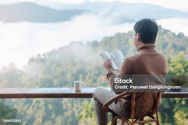Young Man Reading Book Near Window And Looking Mountain View At Countryside Homestay In The Morning Sunrise Solotravel Journey Trip And Relaxing Concept Stock Photo - Download Image Now