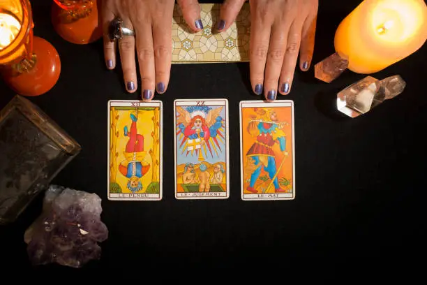 Detail of a woman's hands showing three tarot cards face up, on a black card table. Concept of divination session with tarot cards. View from above.