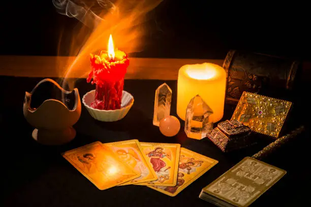 Still life with tarot cards, candles, incense and other objects on a black card table, during a divination session. Concept of a divination session with tarot cards.