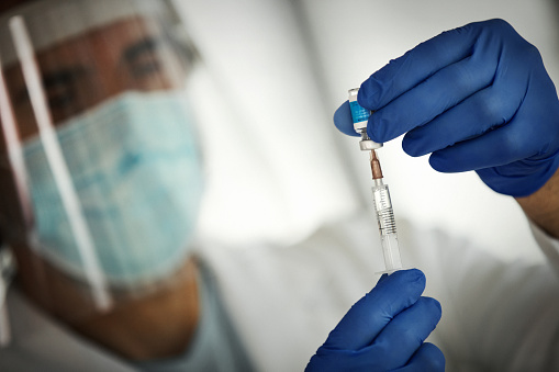 Closeup front view of an adult medical worker preparing COVID-19 vaccine to br administred. \n\nNOTE: label is imaginary