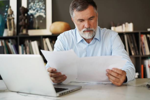 istock Serious mature male employee sits at the table in modern office, works with documents 1366936723