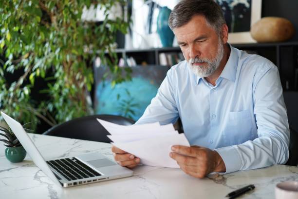 istock Serious mature male employee sits at the table in modern office, works with documents 1366936728