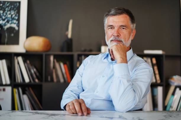 mature professional businessman looking at camera and smiling. confident entrepreneur, leader, manager sitting in office - businessman mature adult 50s men imagens e fotografias de stock