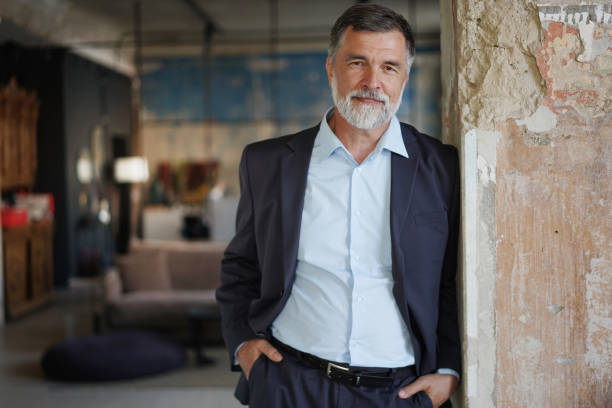 Positive confident mature executive man smiling and looking at camera while standing in office