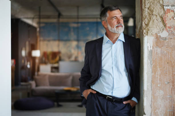 istock Positive confident mature executive man smiling and looking away while standing in office 1366936792
