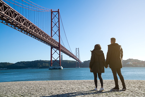 unrecognizable young couple on the 25th of april bridge on a sunny day, lisbon, portugal