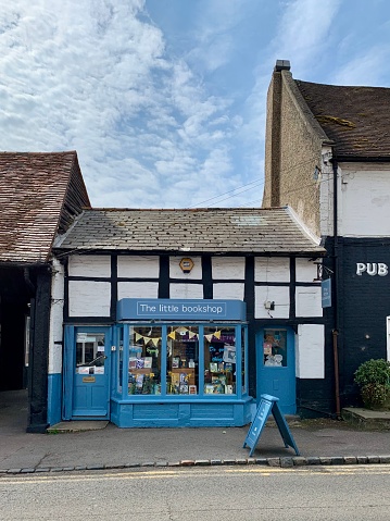 Street view of old town. Small cozy bookshop with blue door and shop window is allocated in medieval half timbered house on a High Road. Blue sky.