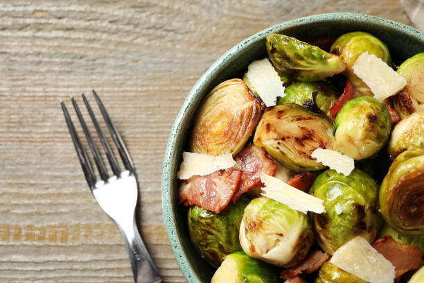 istock Delicious fried Brussels sprouts with bacon in bowl and fork on wooden table, flat lay 1366939379