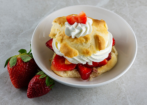 Top side view of a Strawberry Shortcake with whipped cream.  Two additional whole berries on side of bowl.